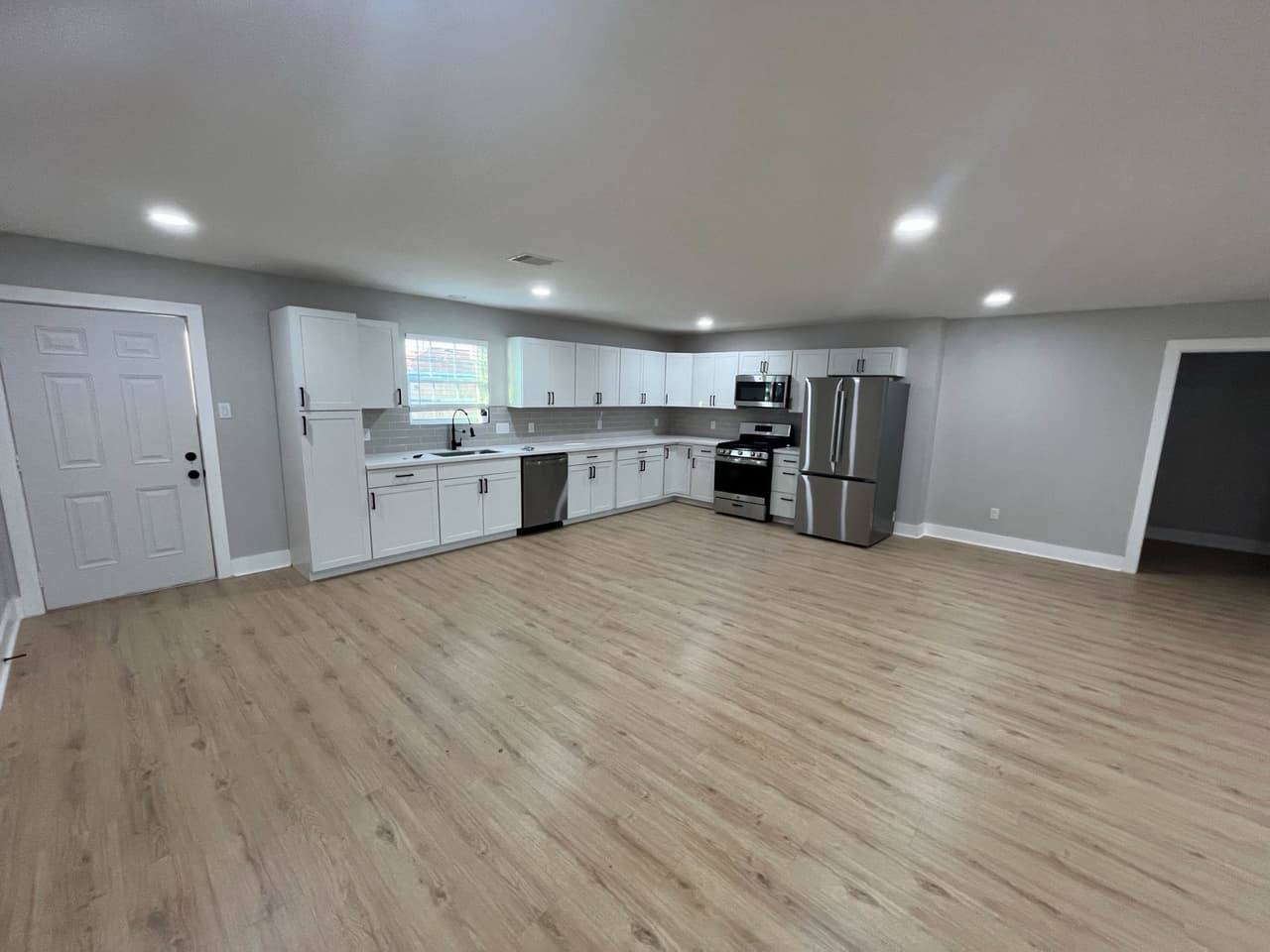 Renovated open kitchen and living area with new white cabinets, stainless appliances, and wood-look flooring.
