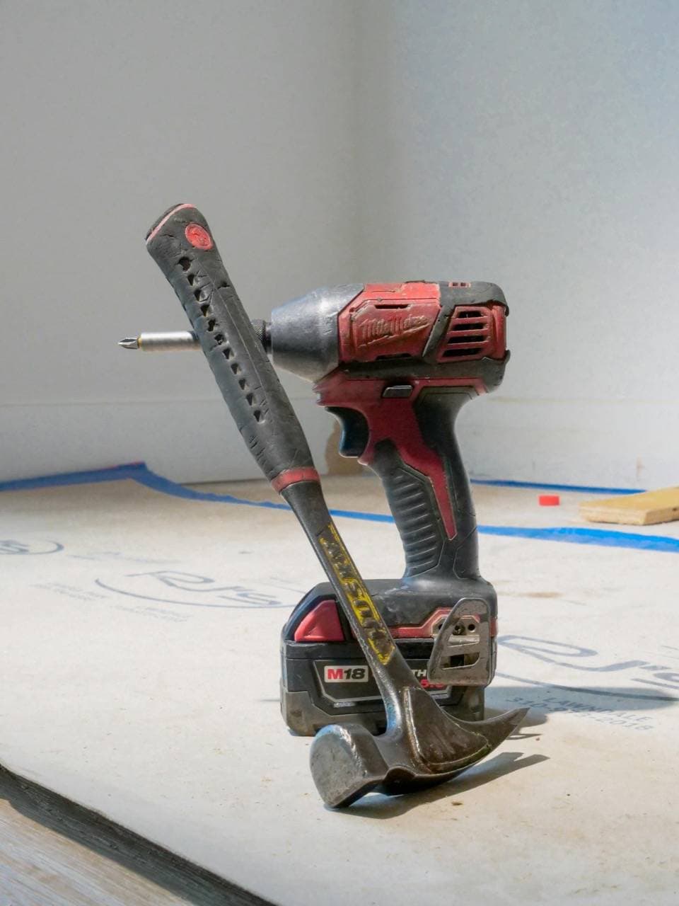 A hammer and power drill on a wooden surface at a construction site.