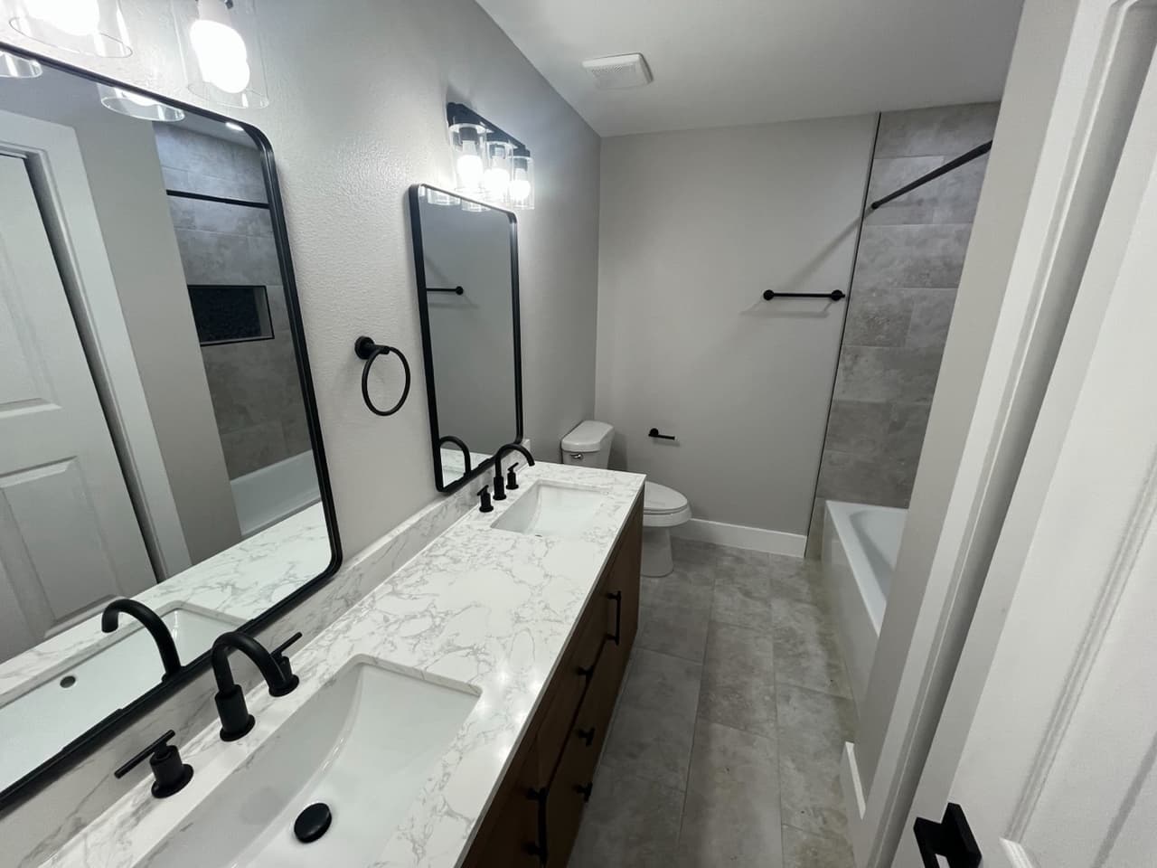 Finished primary bathroom with a double vanity, marble-look countertops, and a tiled tub surround